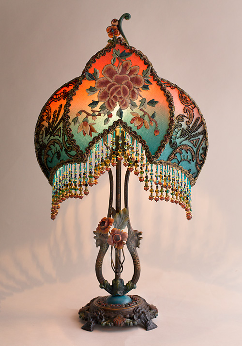 The shade is covered with antique textiles including antique metallic lpatterned ace and ornately beaded 1920s flapper dress remnants. The front panel features a finely embroidered antique Chinese Peony applique and the surrounding trim is inset with wonderful multicolored beaded passimenterie while the sides of the shade are covered with colorful floral net trim.